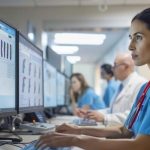 A medical professional is reviewing digital data on multiple computer screens, focusing on medical imaging and patient records in a modern healthcare setting.