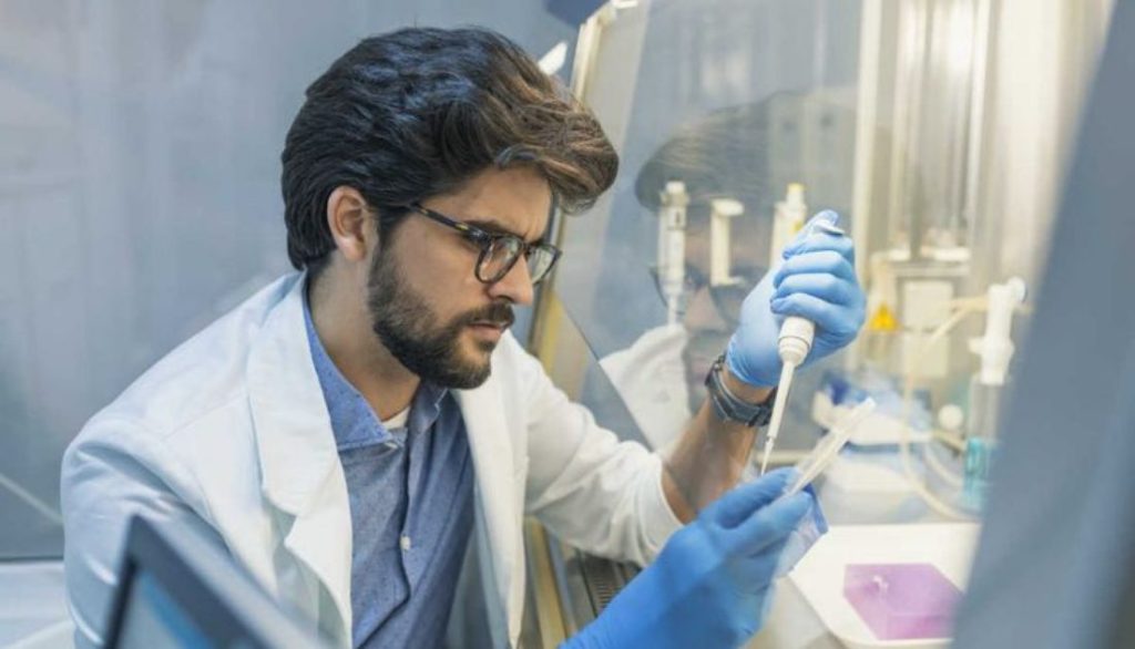 Laboratory scientist in a lab coat and gloves using a pipette inside a clean lab workspace while preparing samples for testing.