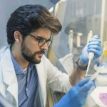 Laboratory scientist in a lab coat and gloves using a pipette inside a clean lab workspace while preparing samples for testing.