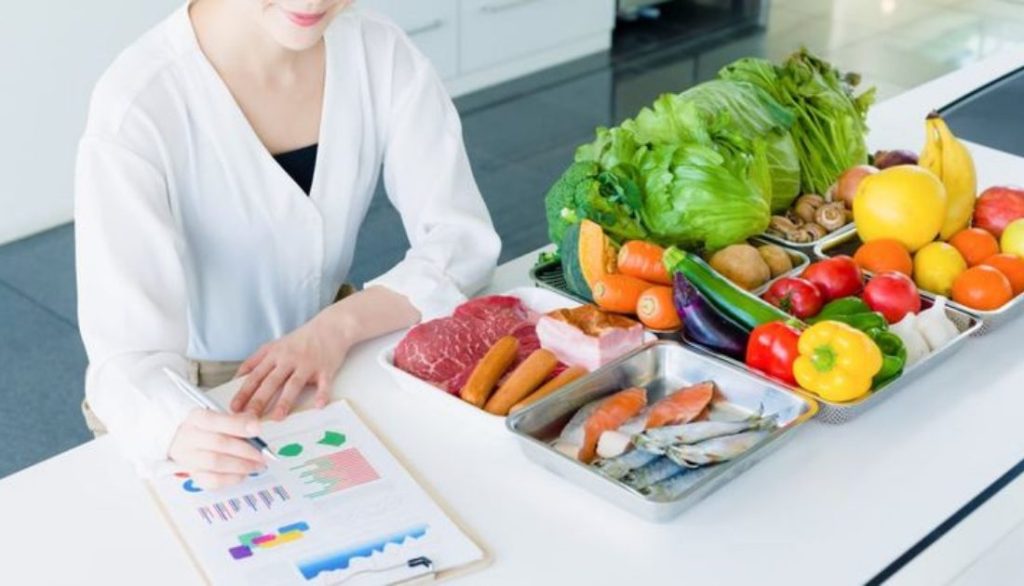 Food compliance professional reviewing inspection notes beside assorted fresh produce and packaged meats on a kitchen counter.