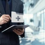 A professional in a suit using a tablet with a digital medical folder icon. This represents a modern FDA inspector or quality manager conducting a digital GMP audit in a clean, corporate facility.